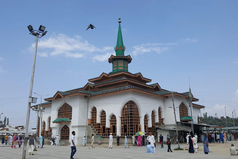 Visitors walk next to a white building with a tiered roof and tall green spire.