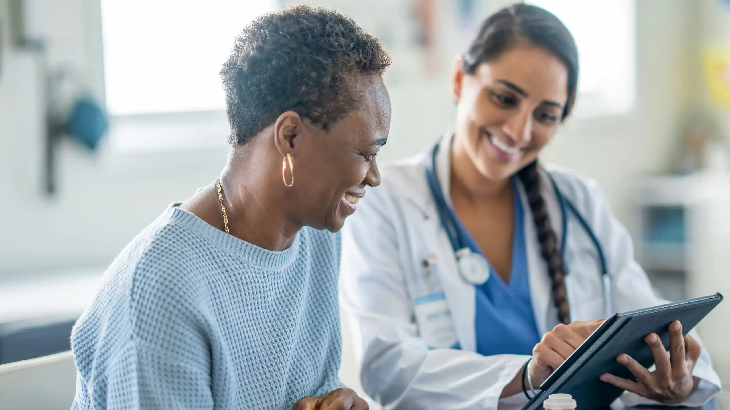 A woman in a white coat with a stethoscope shows a clipboard to another woman