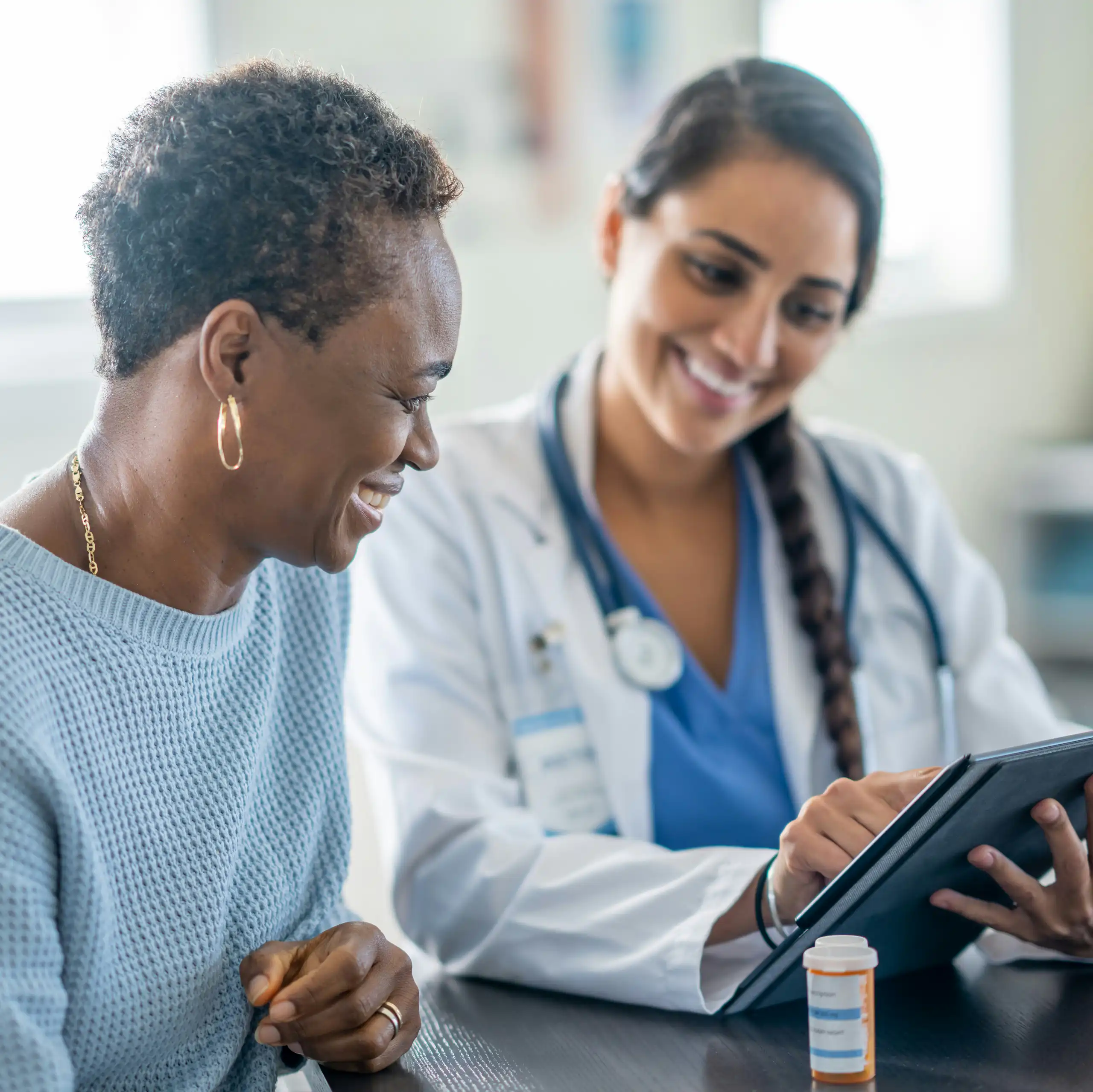 A woman in a white coat with a stethoscope shows a clipboard to another woman
