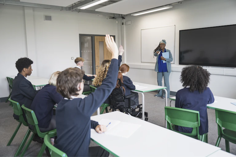 A teenage student puts their hand up to answer a teacher's question