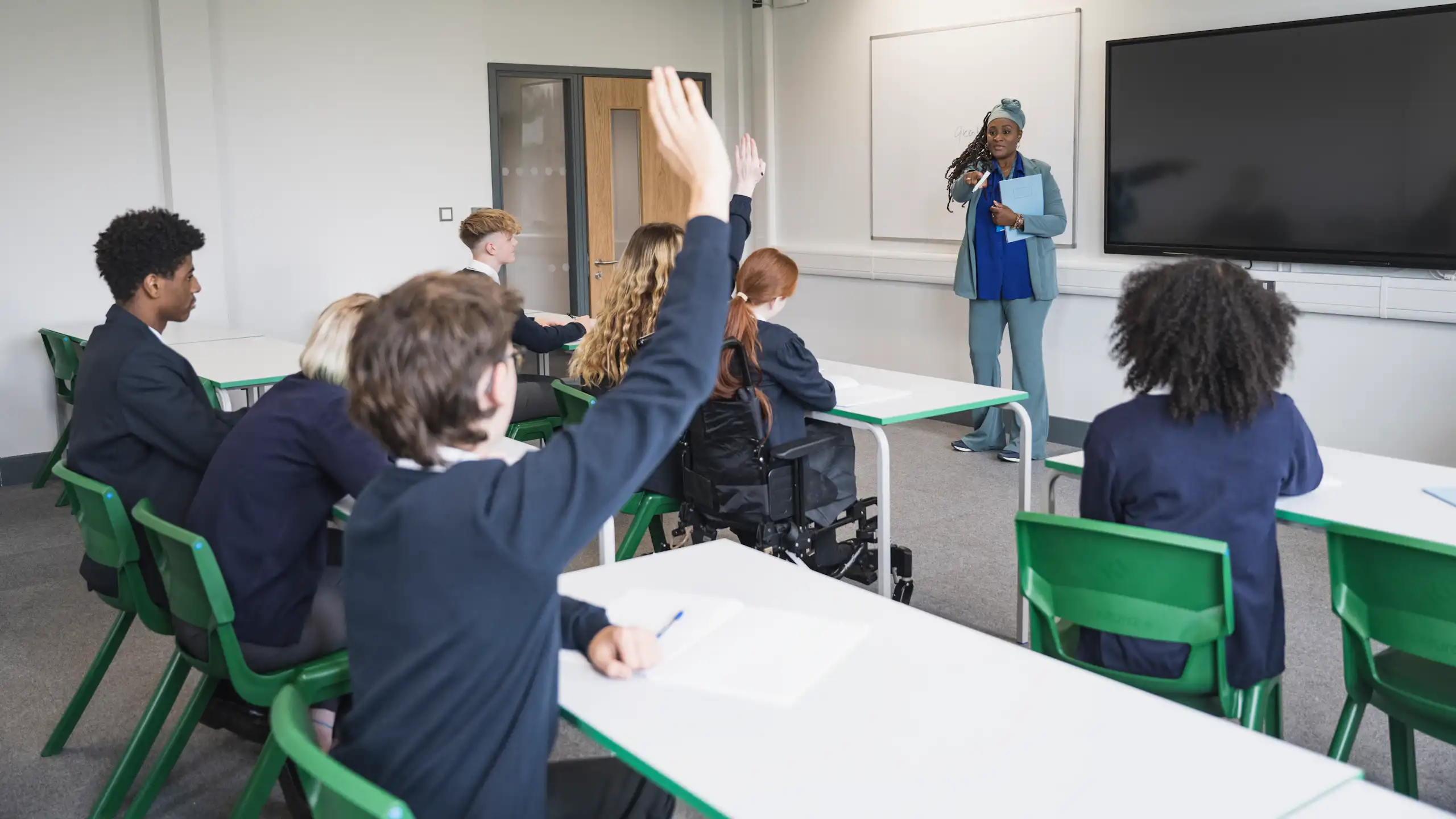 A teenage student puts their hand up to answer a teacher's question
