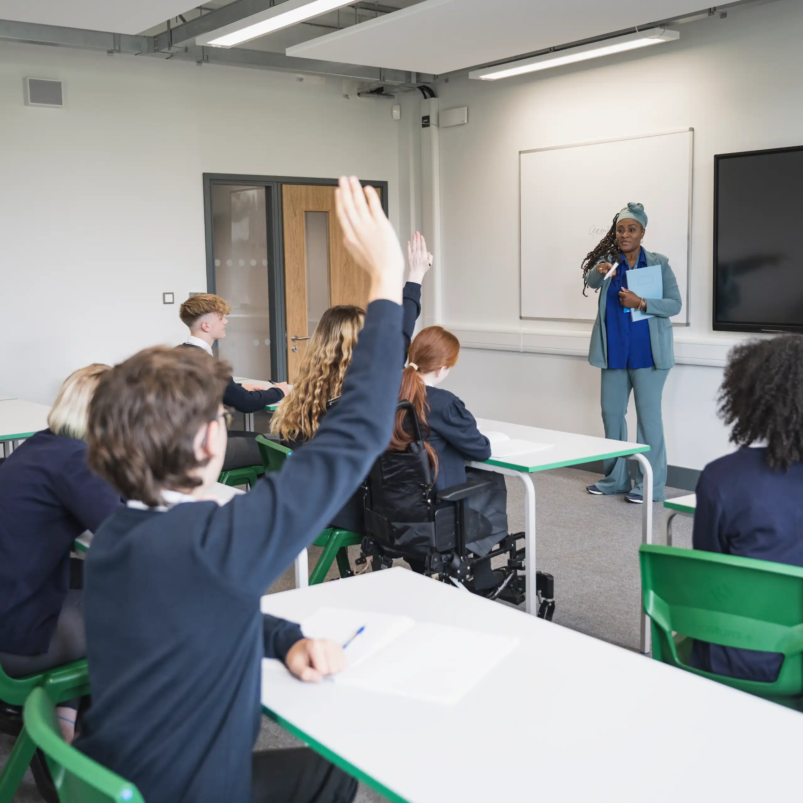 A teenage student puts their hand up to answer a teacher's question