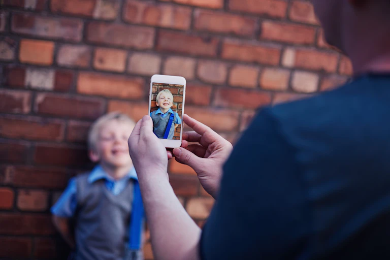 An adult takes a photo on a phone of a young child.