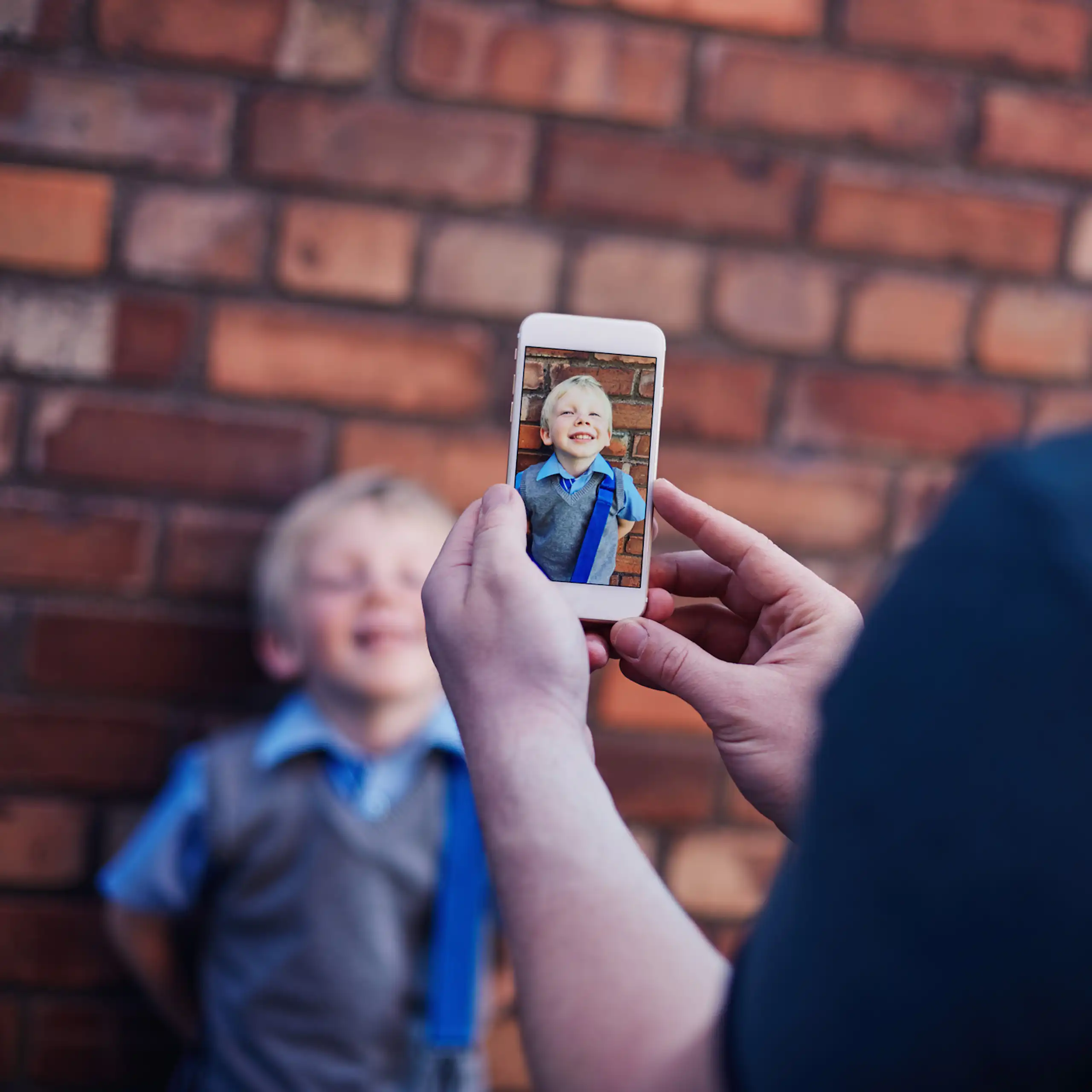 An adult takes a photo on a phone of a young child.