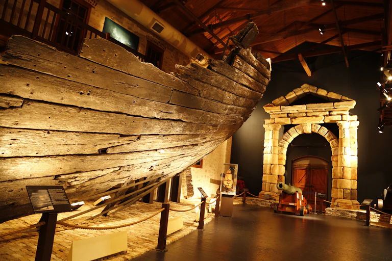 A weathered timber ship hill in a museum, alongside a stone archway.