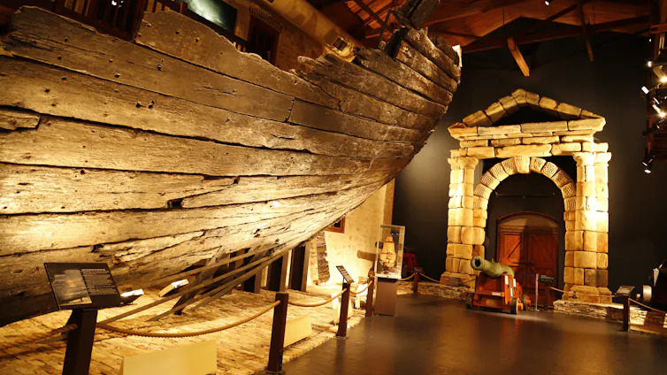 A weathered timber ship hill in a museum, alongside a stone archway.