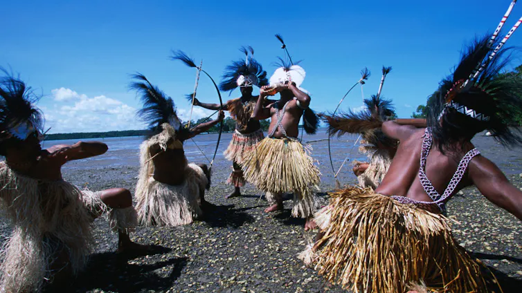traditional dancers with feathered headdresses on a beach from the Torres Strait.