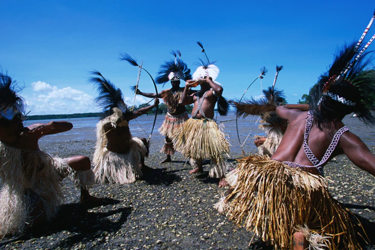 traditional dancers with feathered headdresses on a beach from the Torres Strait.