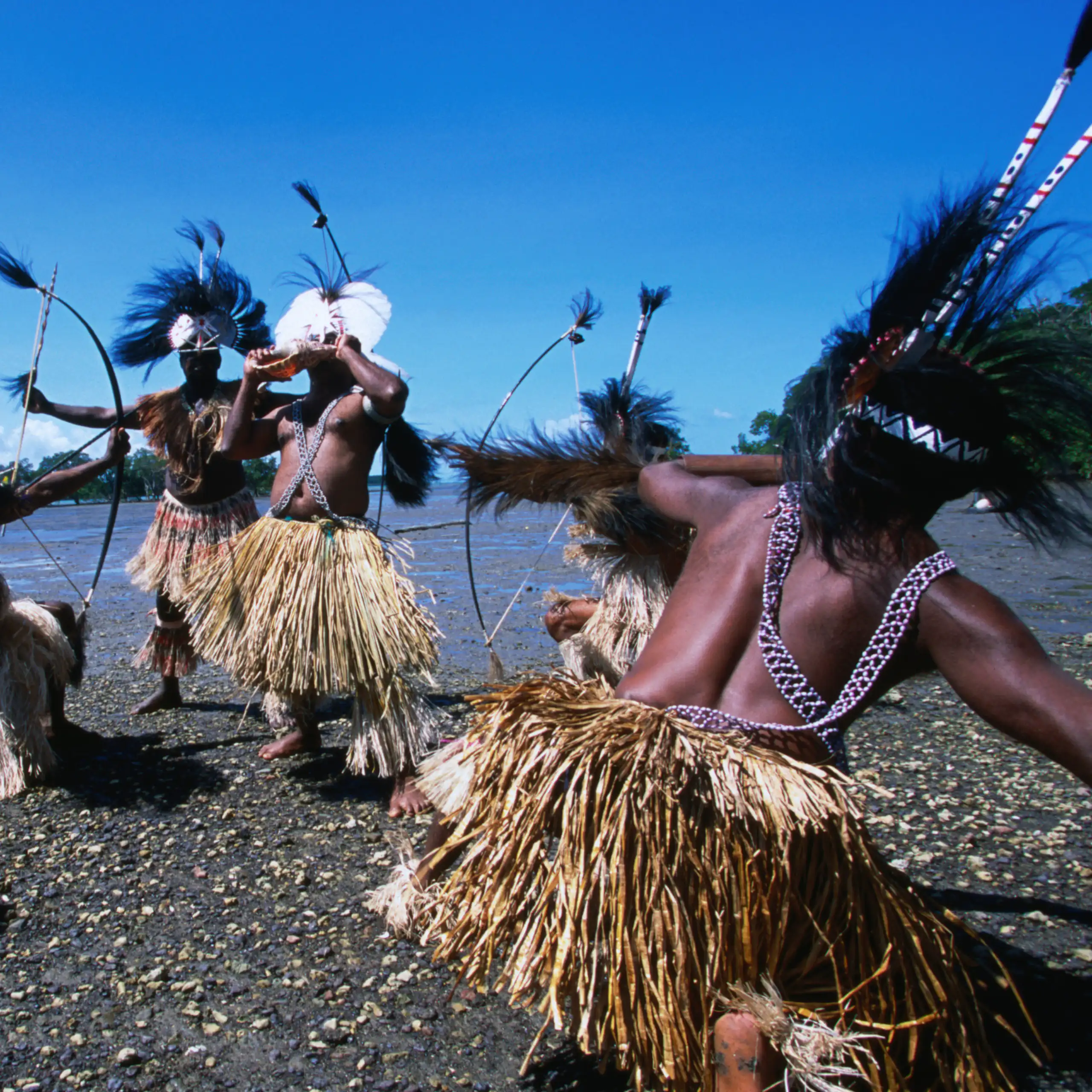 traditional dancers with feathered headdresses on a beach from the Torres Strait.