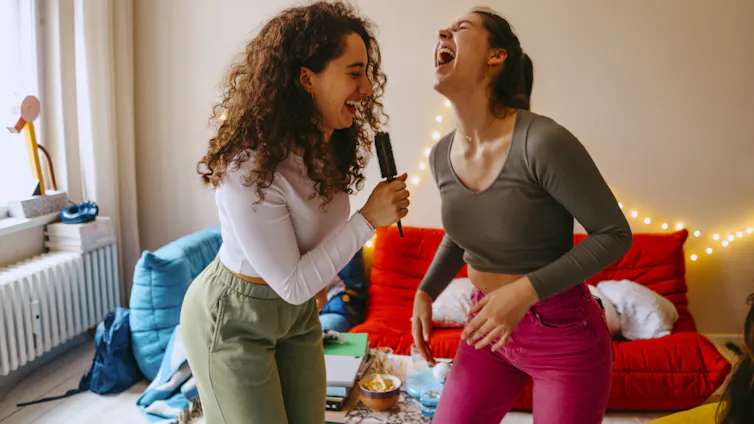 Laughing women singing into hair brush.