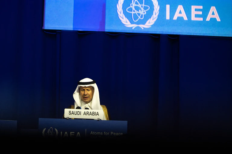 A man sits at a lectern in front of a large screen with IAEA written on it.