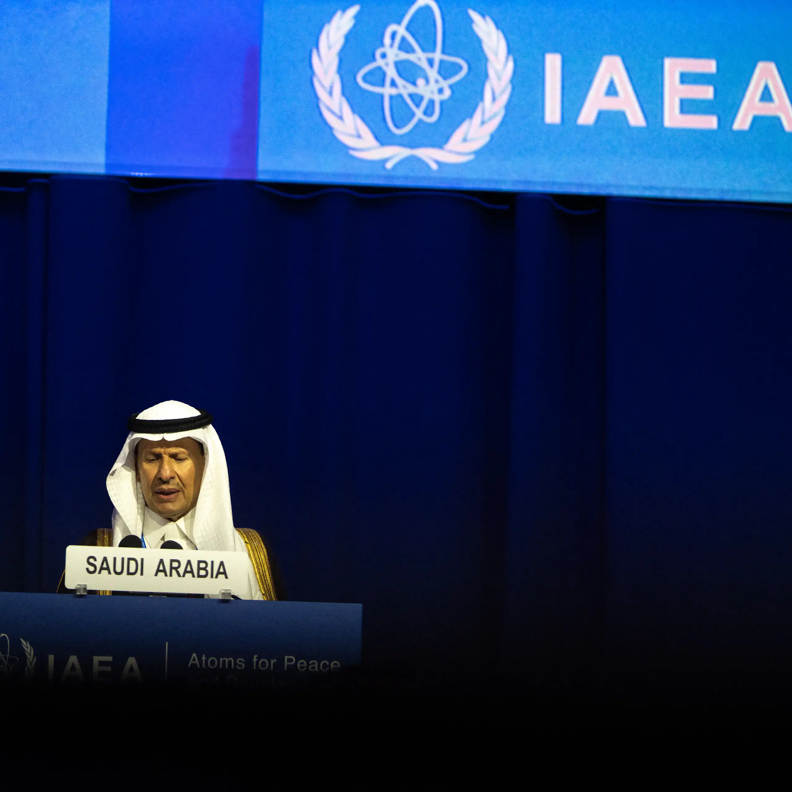 A man sits at a lectern in front of a large screen with IAEA written on it.