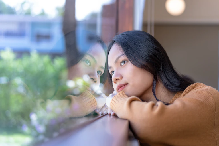 A woman daydreams while staring out the window.