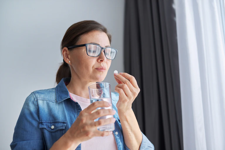 A woman taking a pill with a glass of water.