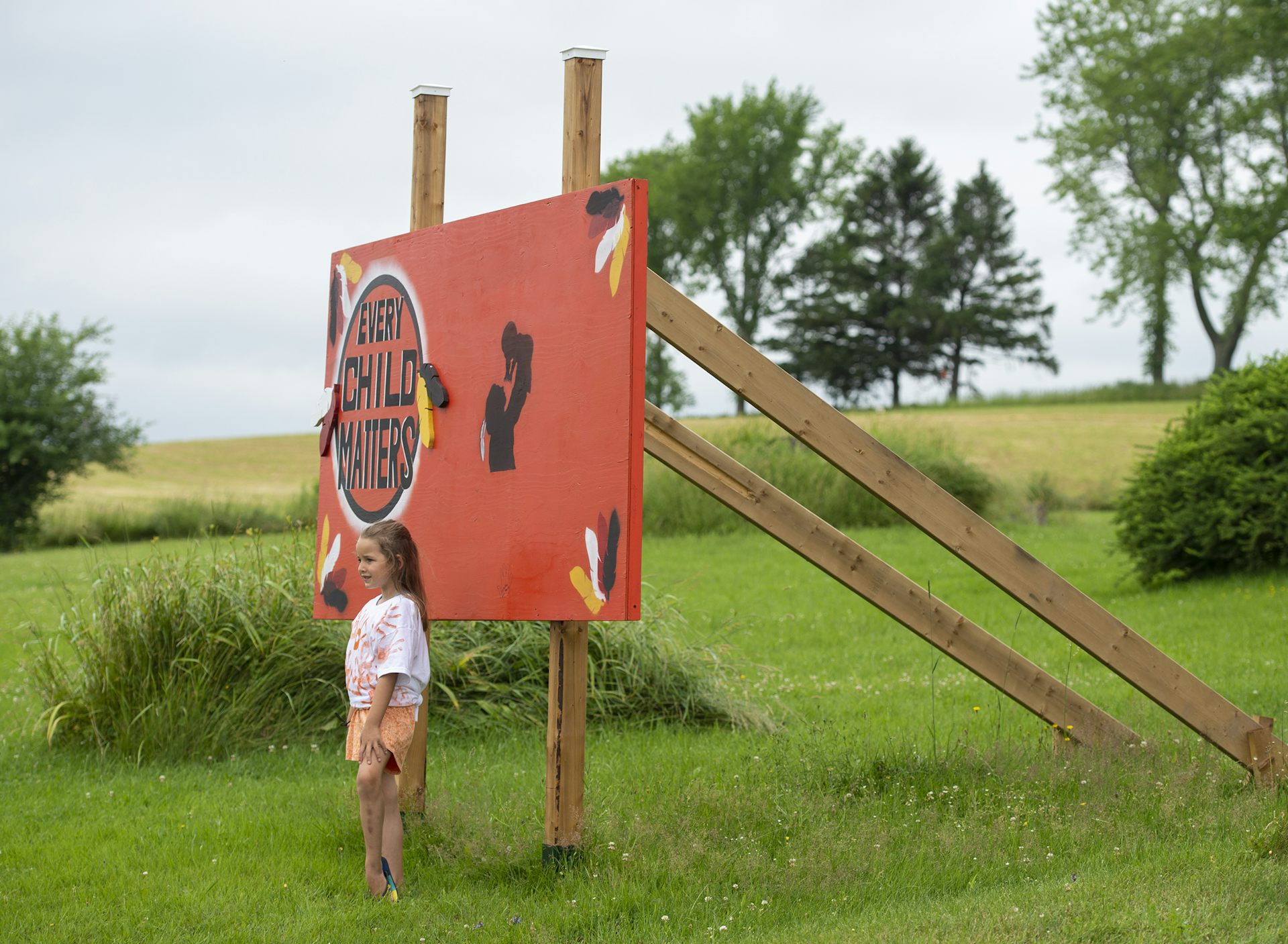 A girl stands in front of an orange sign in a rural area.
