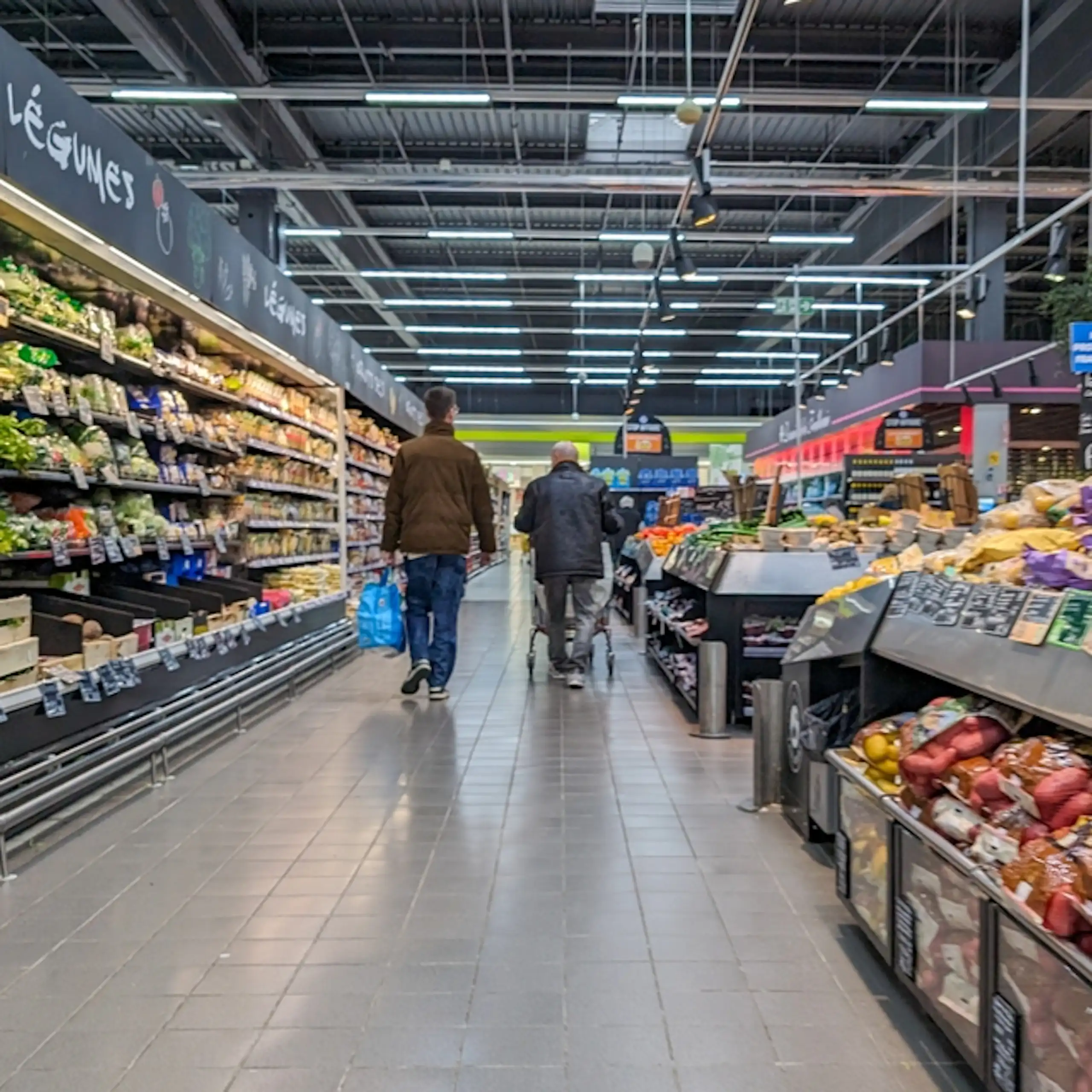 Deux personnes de dos dans l'allée d'un supermarché.