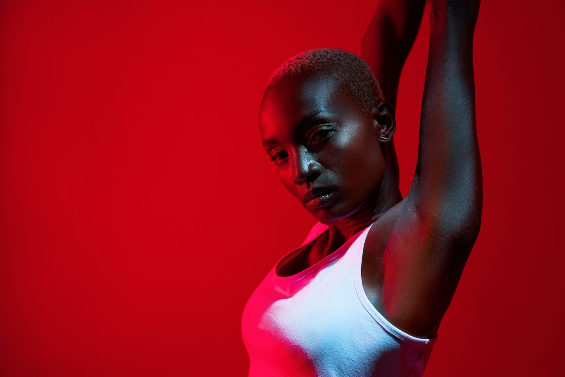 Close up, cropped image of woman in white vest stretching her arms above her head in infrared lighting