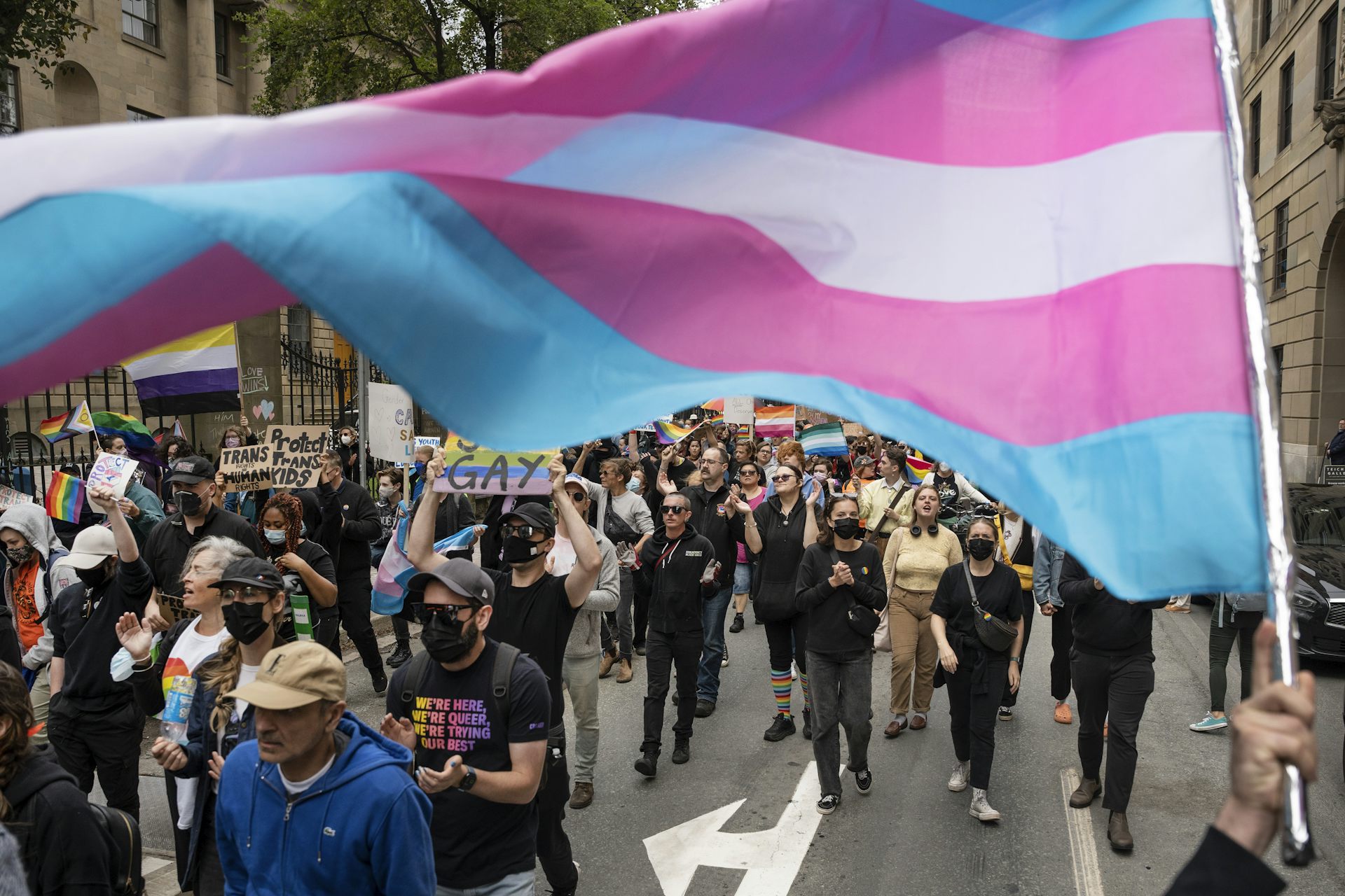 A group of people marching down a street with a flag raised above them.