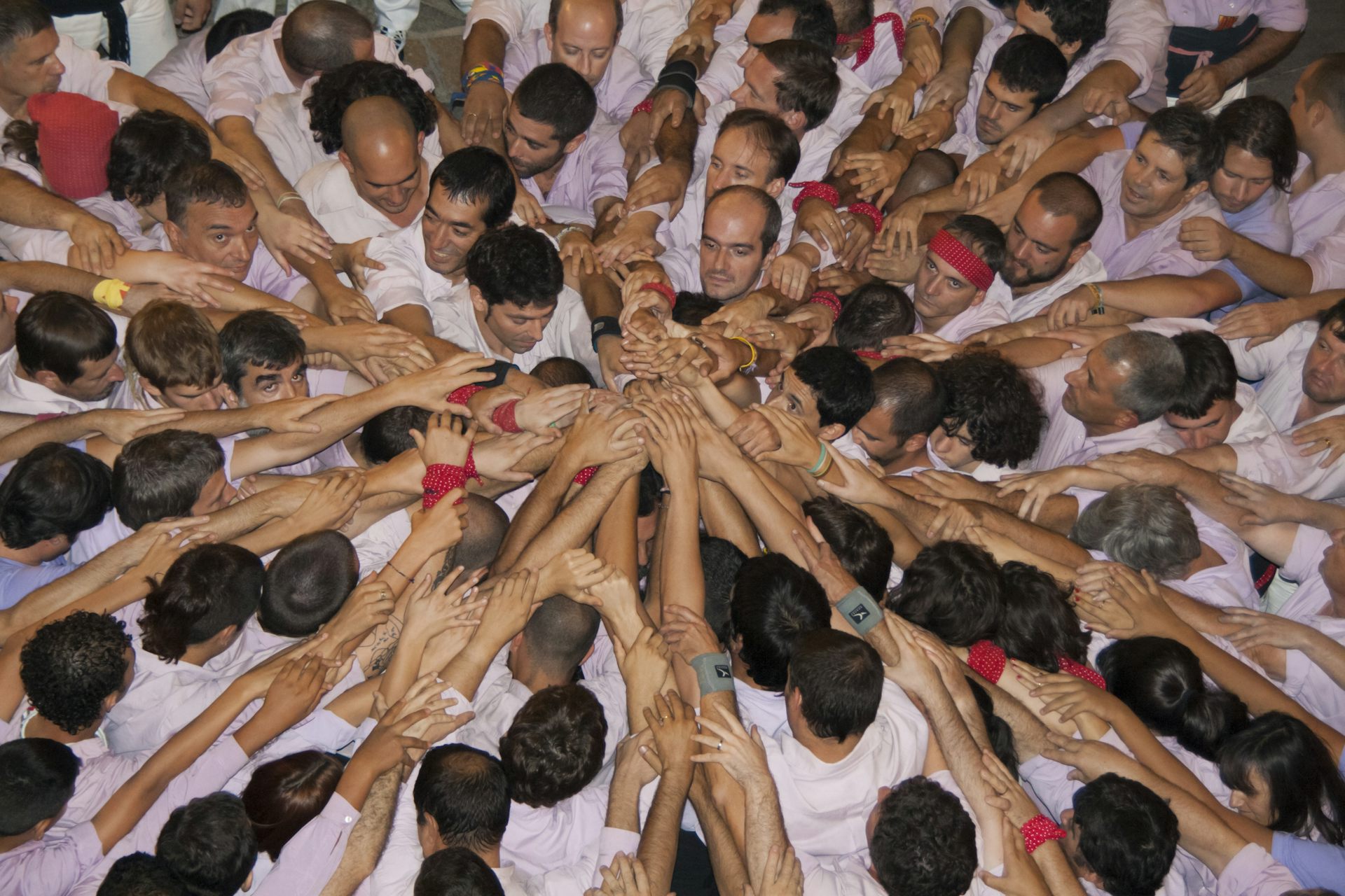 Una colla de castellers fa pinya al terra, juntant totes les mans al centre.