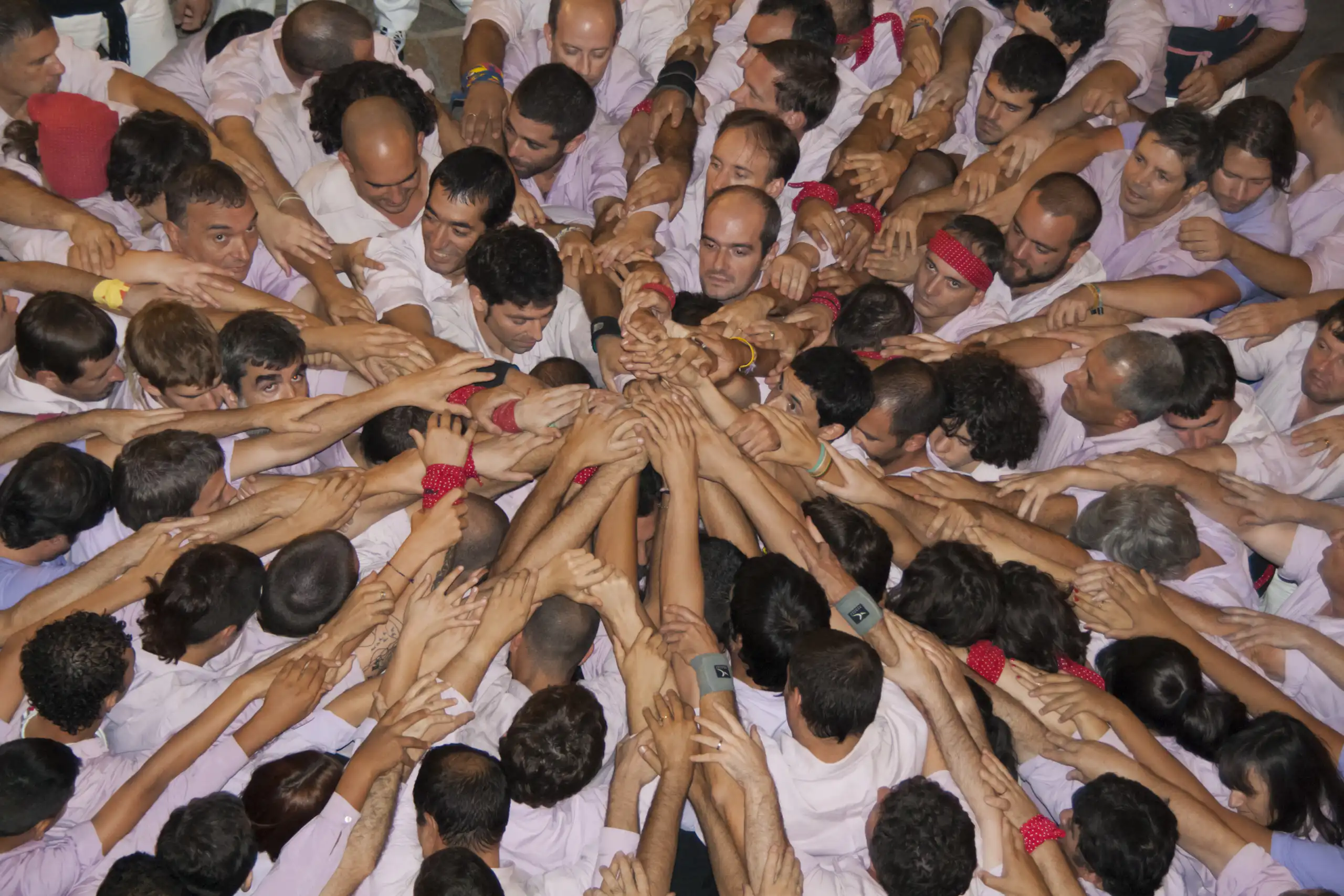 Una colla de castellers fa pinya al terra, juntant totes les mans al centre.