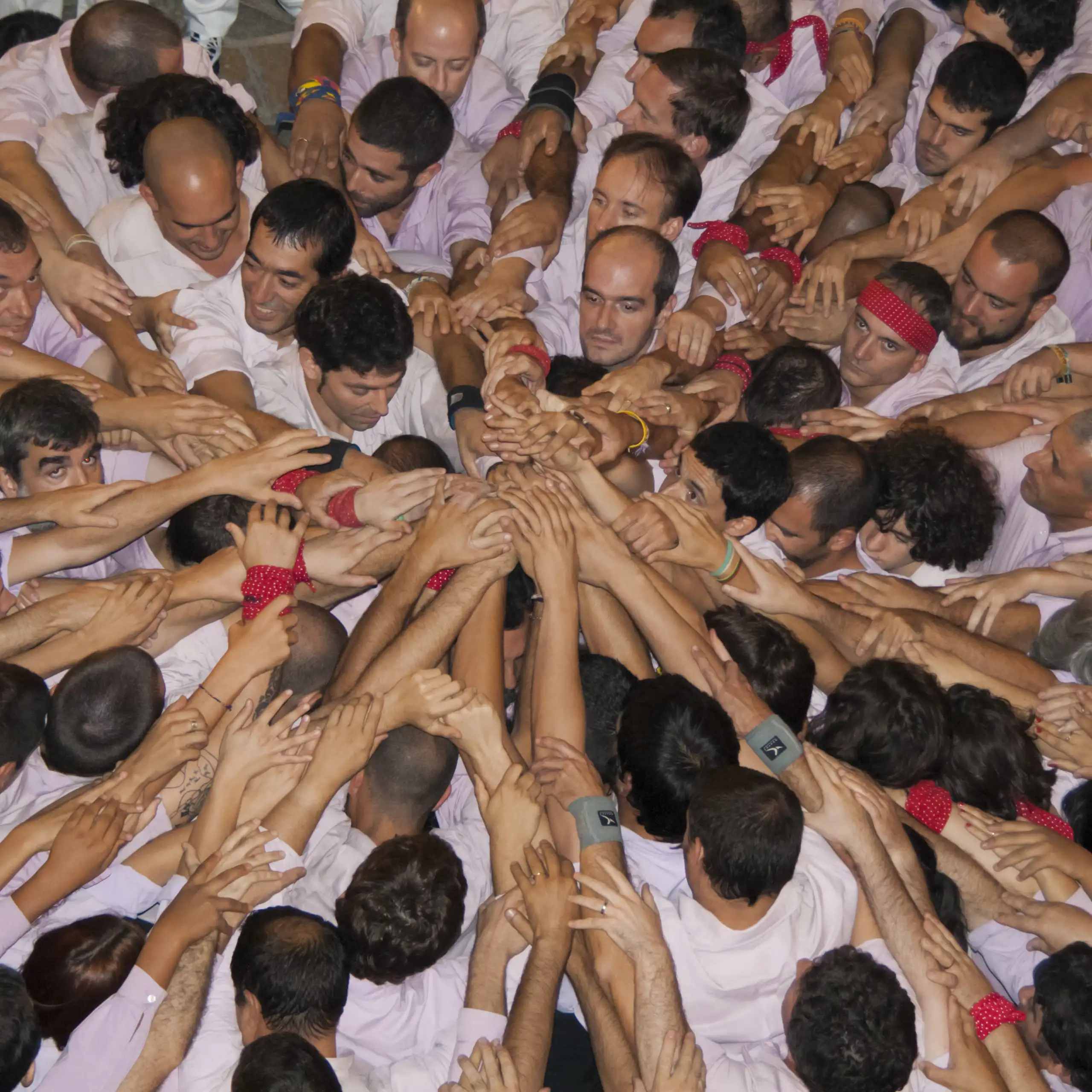 Una colla de castellers fa pinya al terra, juntant totes les mans al centre.