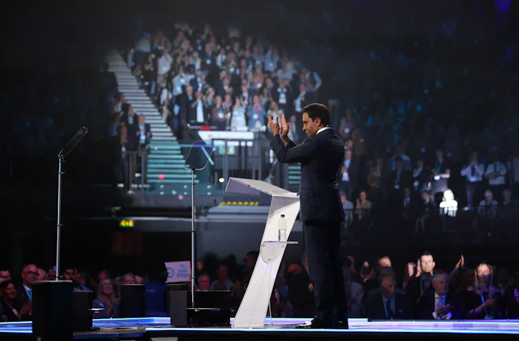 zia yusuf on stage applauding the crowd at reform uk conference in 2024.