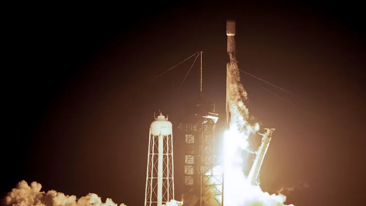 A rocket lifting off a launchpad, with a plume of flame and smoke below it.