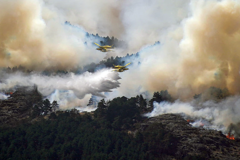 Planes fly over a forest with heavy smoke in the air.
