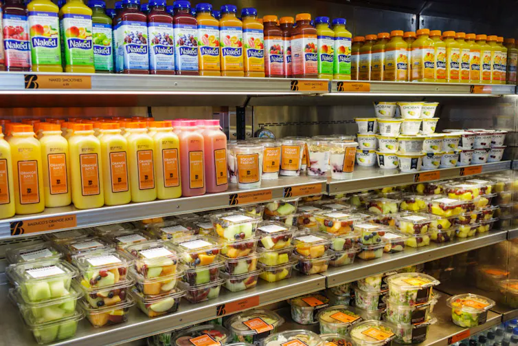 Rows of juice and fresh produce packaged on a convenience store shelf.