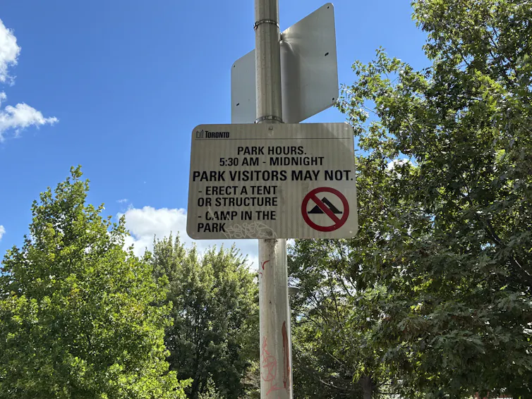 white roadsign stating tents can't be put up in park, green trees in background