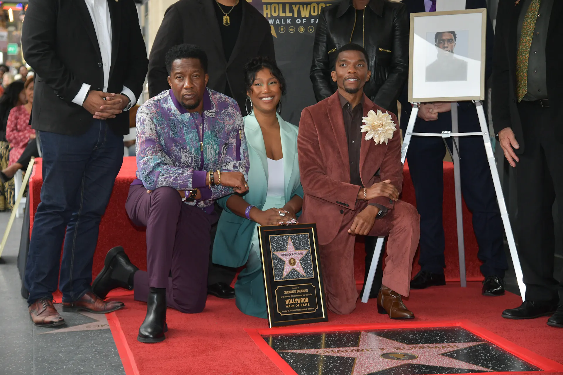 Three people kneel before a star on the sidewalk next to a framed photo of the late actor Chadwick Boseman.