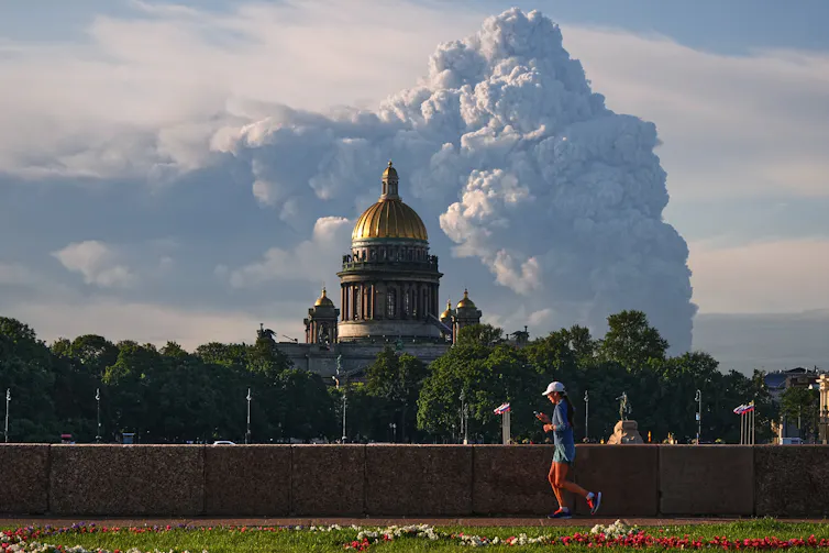 Billowing smoke on the horizon with a runner and a catherdral in the foreground.