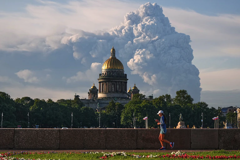 Billowing smoke on the horizon with a runner and a catherdral in the foreground.