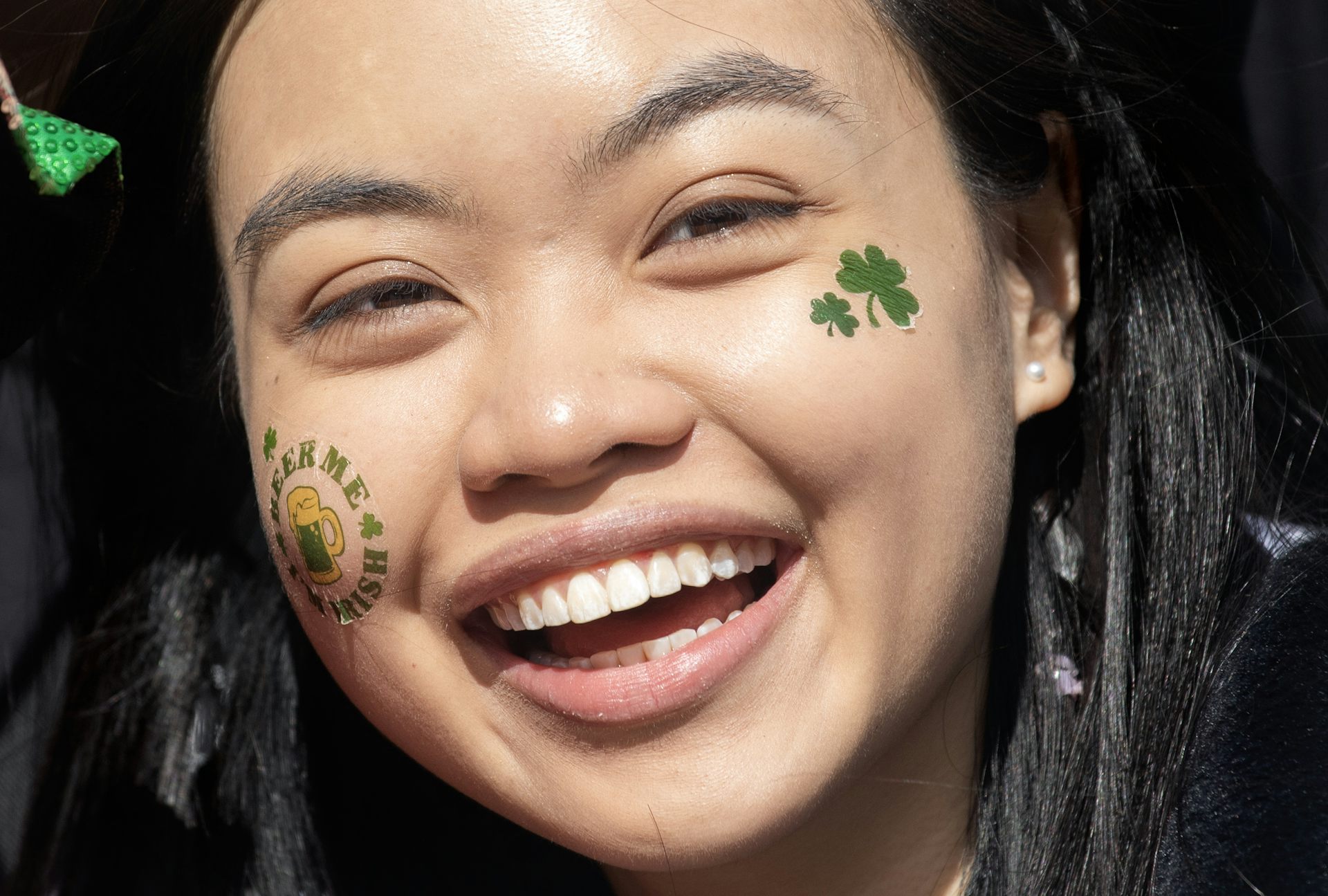 Une jeune femme d’origine asiatique porte des autocollants au visage : un trèfle sur une joue et l’inscription « Kiss me, I’m Irish » sur l’autre