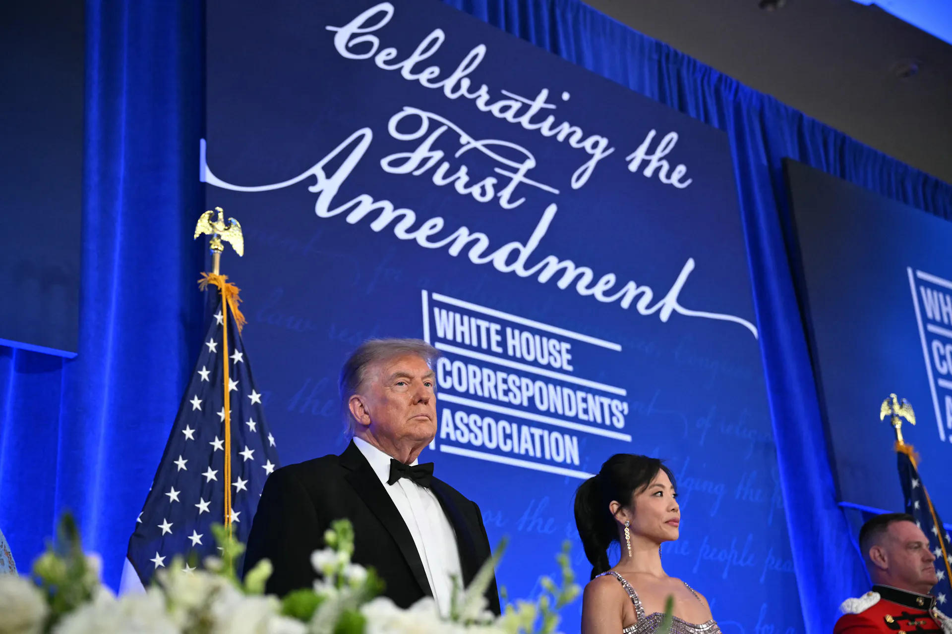 A man and a woman in formal dress stending in front of a banner that says 'Celebrating the First Amendment.'