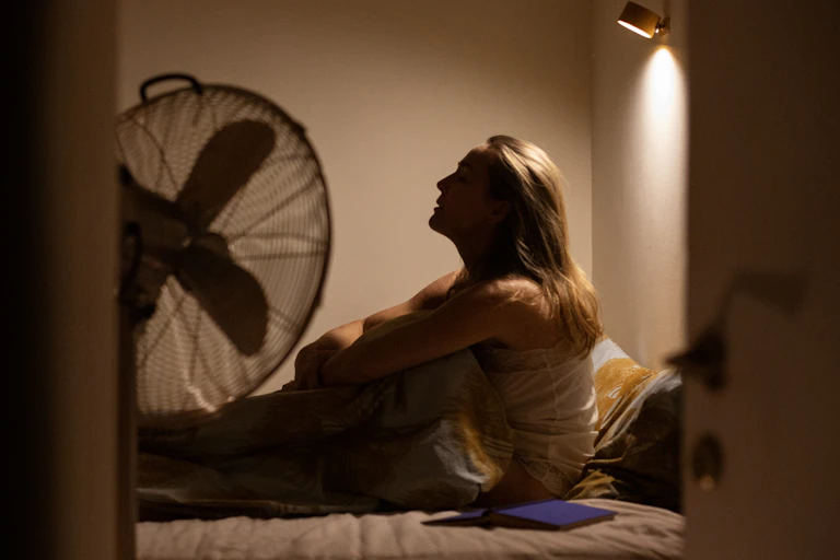Person sitting up in bed facing a fan