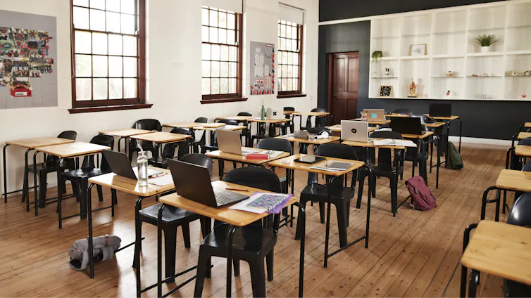 An empty classroom has laptops open on a series of desk lined up in rows.