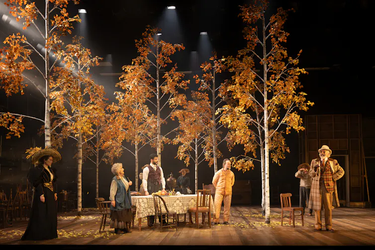 Production image: the cast on stage under autumnal trees.