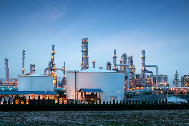 An oil refinery plant lit up in front of a dark blue sky.
