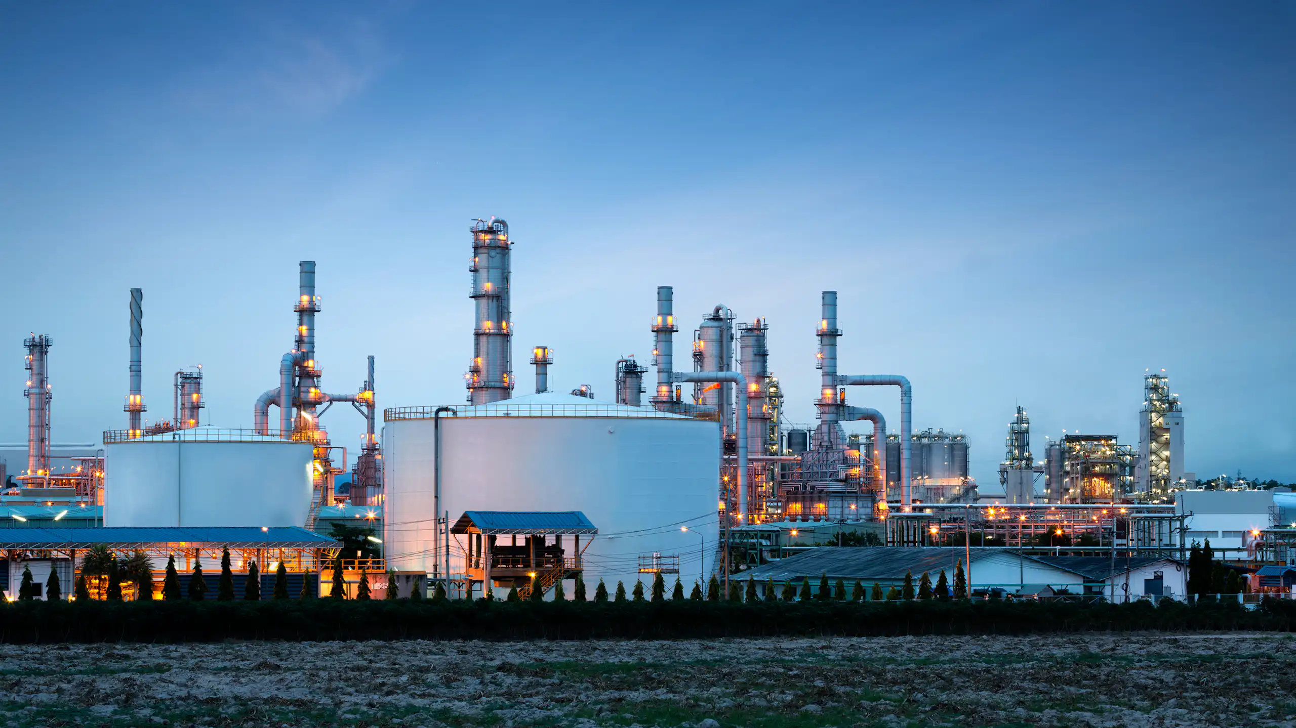 An oil refinery plant lit up in front of a dark blue sky.