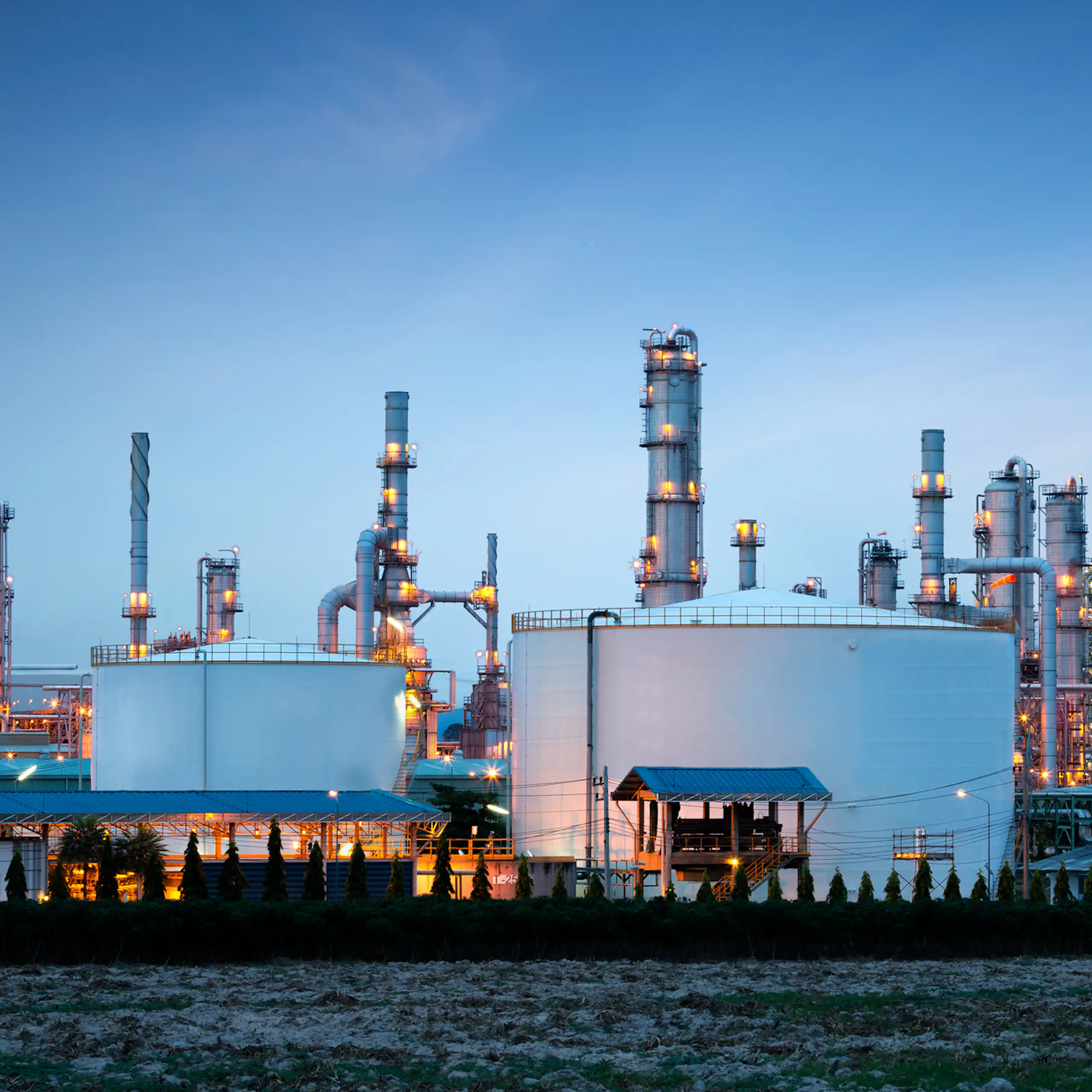 An oil refinery plant lit up in front of a dark blue sky.