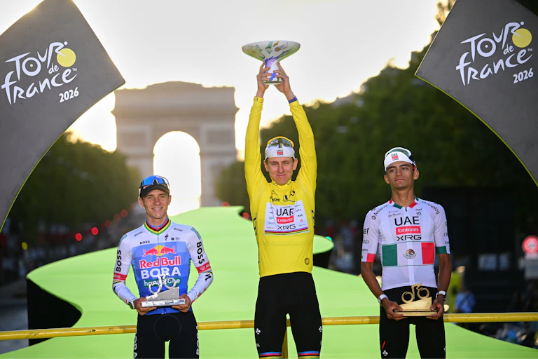 Three men stand on a podium, one holding up a trophy