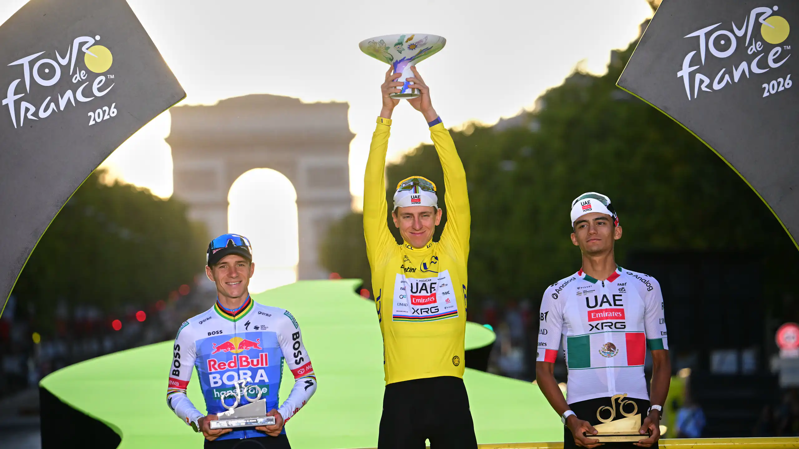 Three men stand on a podium, one holding up a trophy
