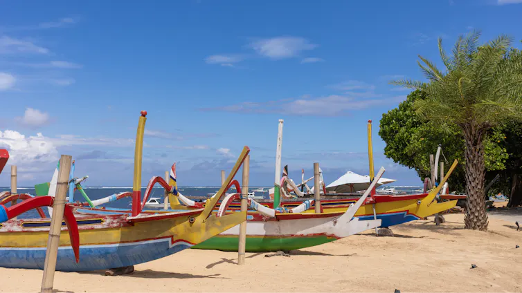 Traditional Balinese boats line a beach.