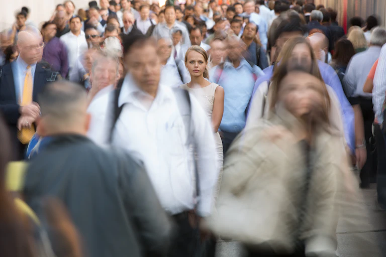 Crowd of people in a big city, commuters going to work, one woman in focus, standing still
