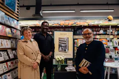 3 people stand next to an enlarged book cover.