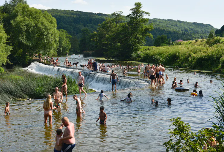 people standing and paddling in river by weir, summer, green trees
