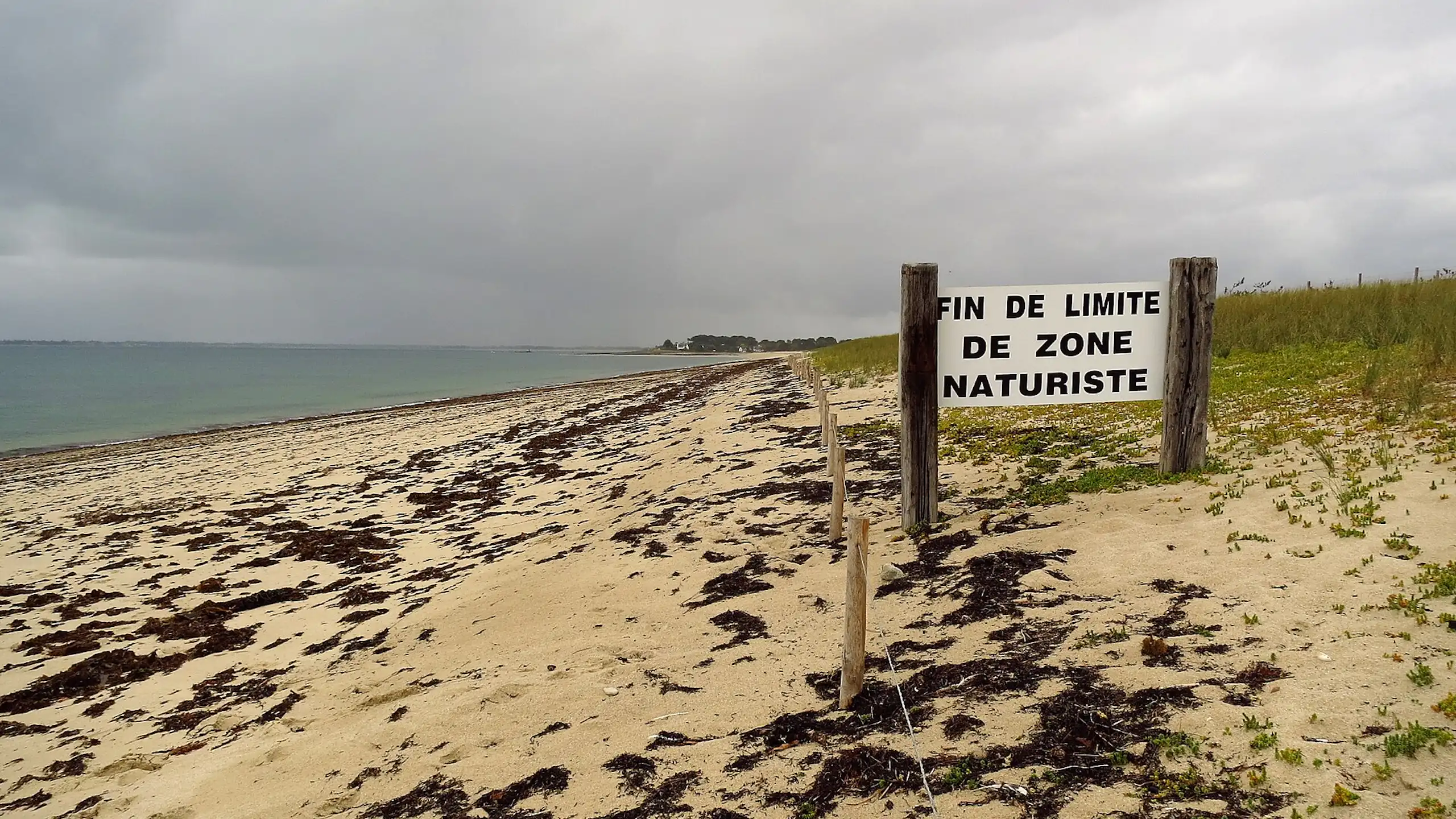 Vue d'une plage avec un panneau à l'entrée annonçant « Fin de limite de zone naturiste ».
