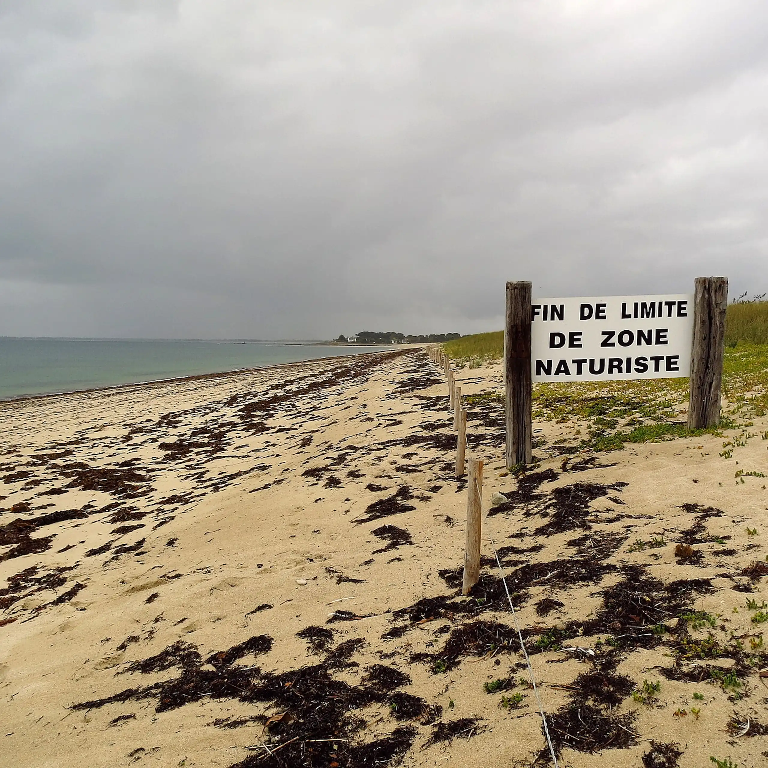 Vue d'une plage avec un panneau à l'entrée annonçant « Fin de limite de zone naturiste ».