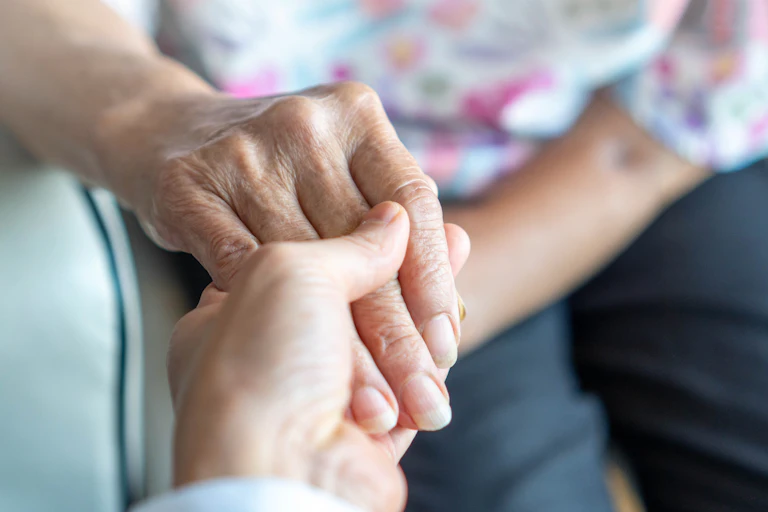carer holding the hand of an elderly woman.